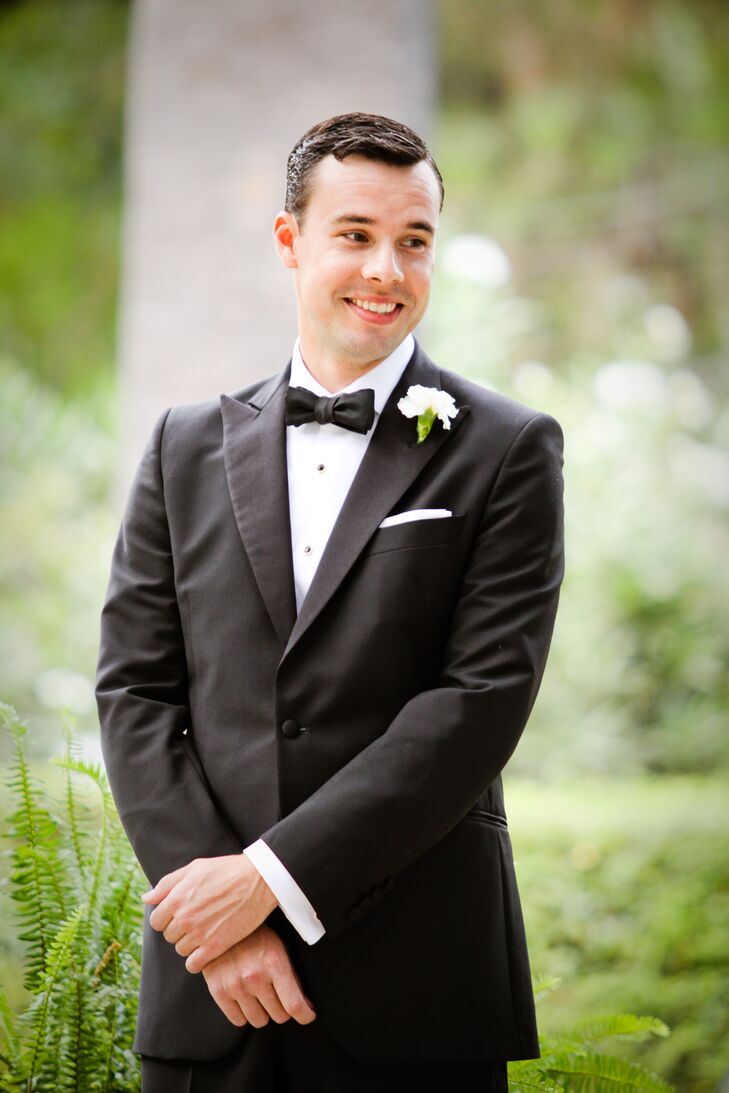 John watched his bride walk down the aisle during the wedding ceremony. He wore a vintage-inspired black tuxedo from the Great Gatsby Collection by Brooks Brothers, with a white button-up dress shirt and a black bow tie.
