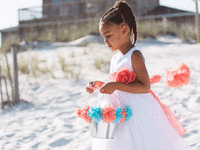 Flower girl walking on sandy beach.