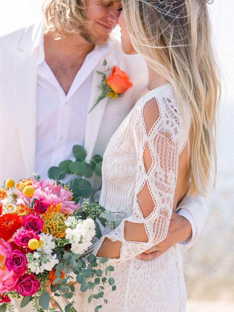 Bride and groom wearing white wedding outfits with pink and orange summer wedding flowers