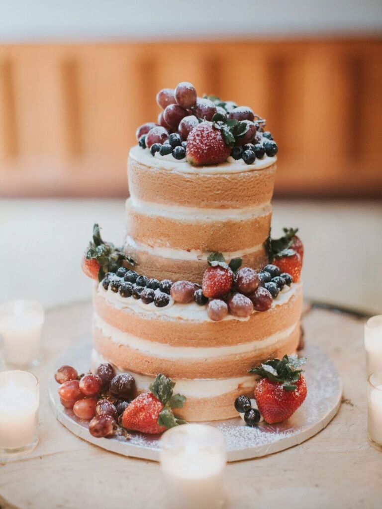naked wedding cake with powdered sugar and blueberries, strawberries and purple grapes