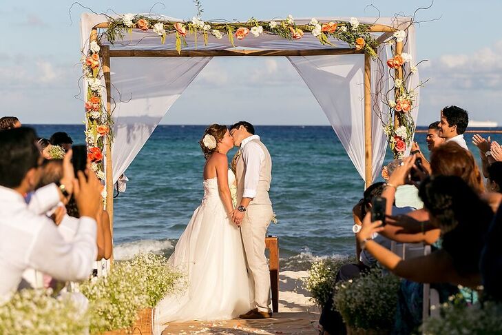 At their beach ceremony, Marta and Jose Luis stood under a wooden arch draped with white linens. Whimsical branches, green hanging amaranthus and white and coral flowers added a romantic touch.