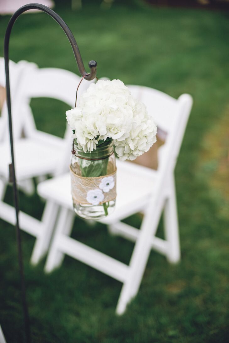 White hydrangeas filled glass hanging mason jars to serve as aisle decorations.