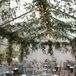 A tented reception space outside Hotel Peter & Paul with hanging greenery, modern chandeliers and small cafe tables with blue linens, gold candles and low centerpieces with pink and blush flowers.