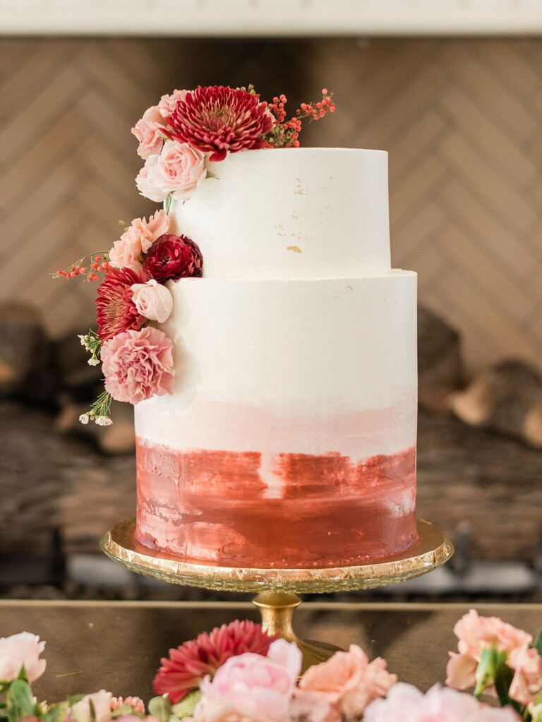two tier white wedding cake decorated with ombre red paint and blush flowers