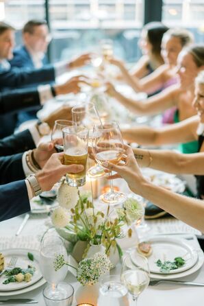 Rehearsal Dinner Guests at Long Table, White Linen Cheers Glasses of Wine, Beer Together to Toast Couple