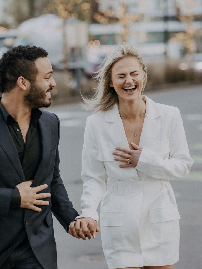 Couple holds hands and laughs while walking down the street. 