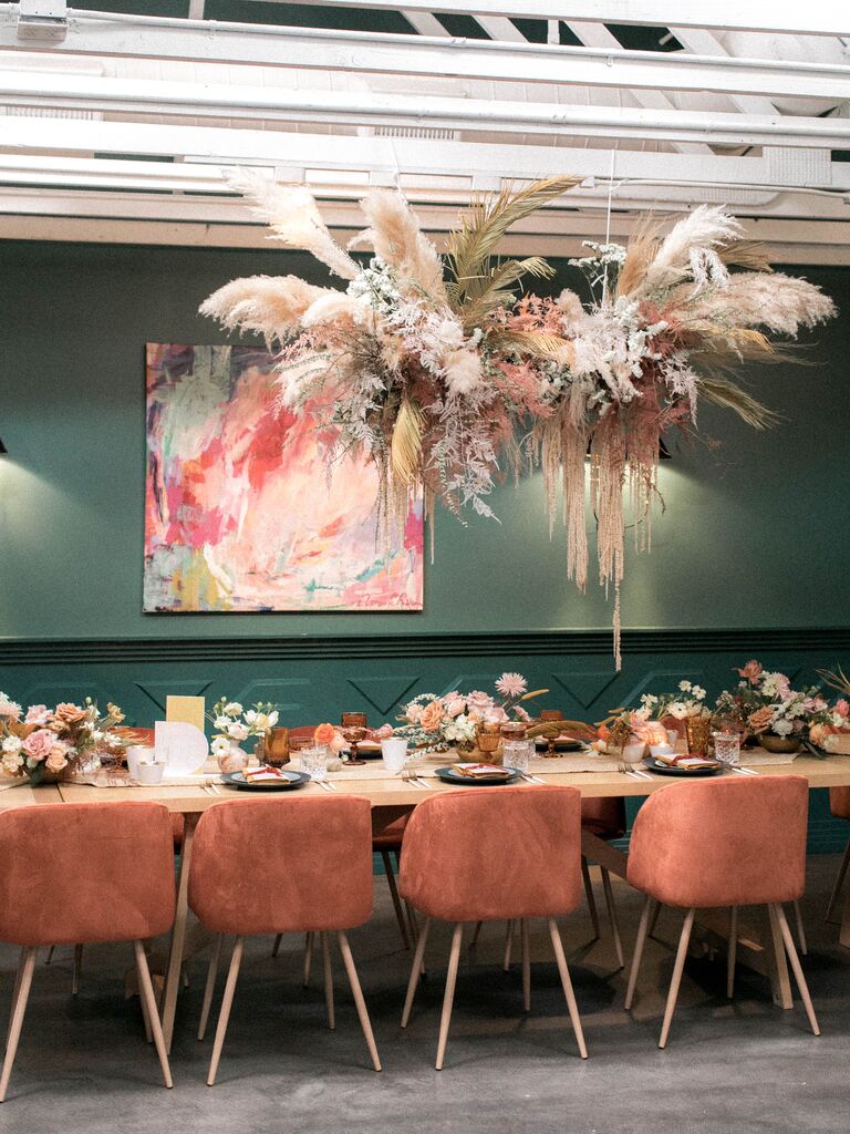 restaurant wedding venue with hanging pampas grass installation above long banquet table with orange velvet chairs