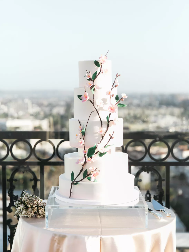A tiered white wedding cake with a sugar-craft branch of cherry blossoms