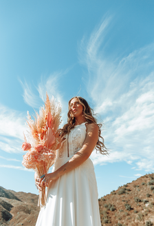 Image looking up at bride in halter wedding dress holding pink dried flowers