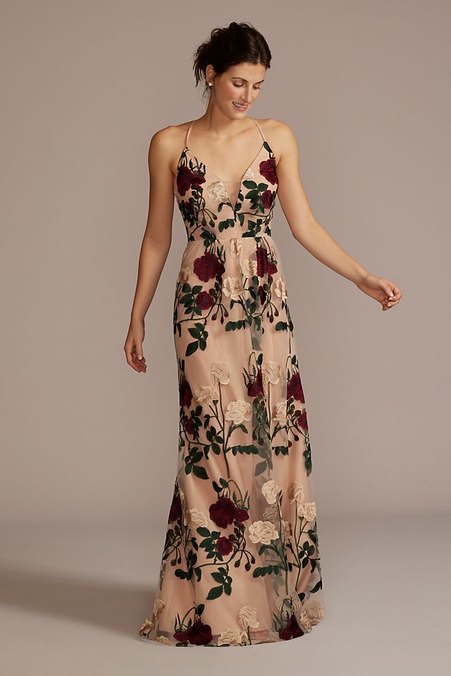 Model wears a floor length nude gown with floral detailing. 