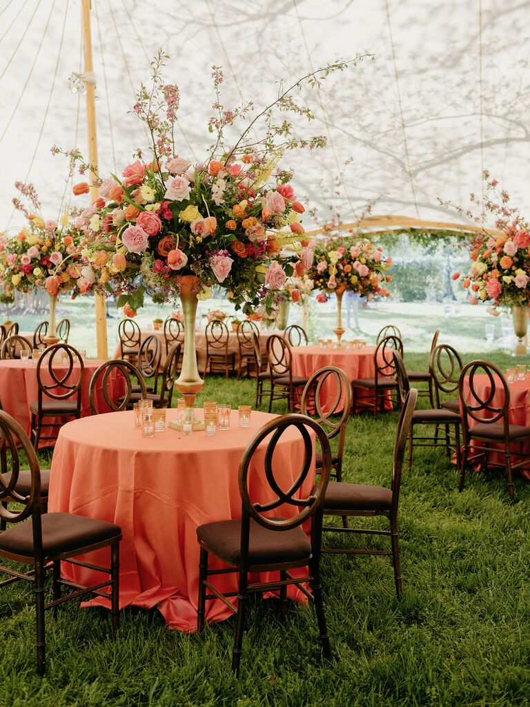 tented wedding reception with round banquet tables decorated with orange tablecloths and tall centerpieces