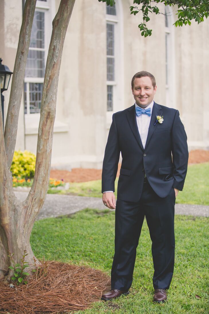 Joshua wore a navy blue suit with a lighter blue bow tie on his wedding day. He pinned an ivory boutonniere to his lapel.