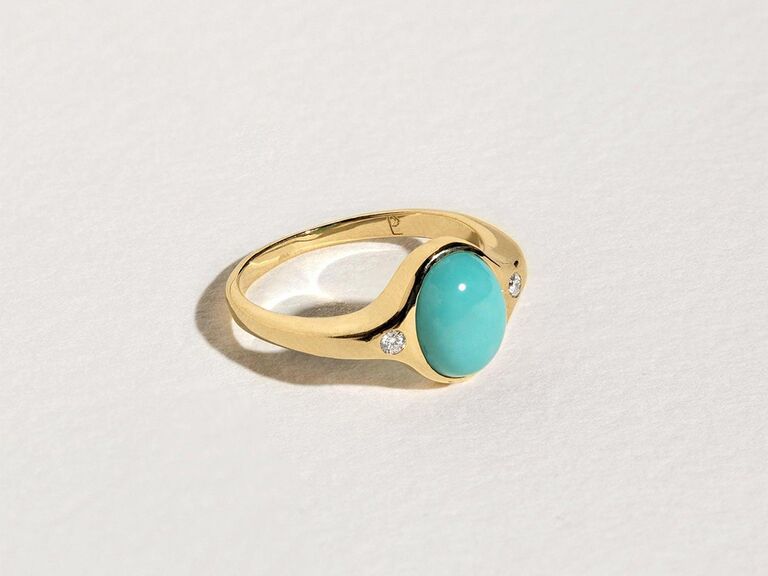 Oval turquoise stone in center bordered by two simple diamonds on thick gold band