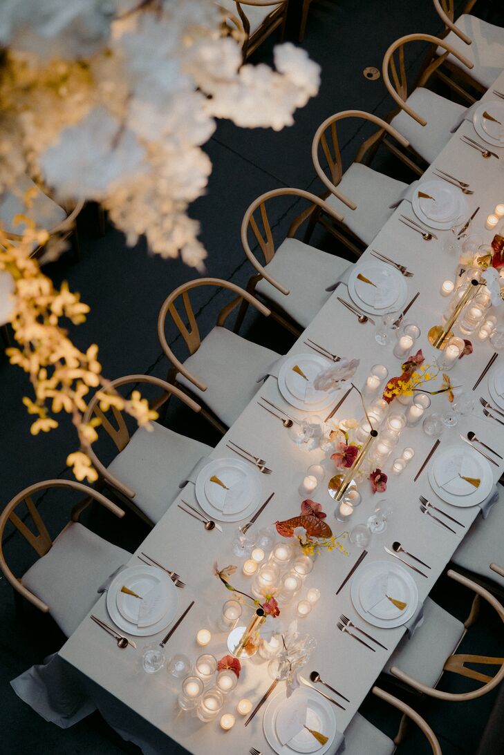 Long Reception Table With neutral Colors, Candles, Simple Centerpieces Under Hanging Flowers Shot From Above