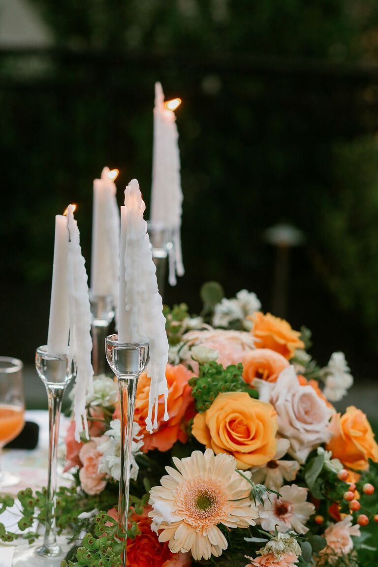 Orange centerpiece with roses and daisies accented by taper candles