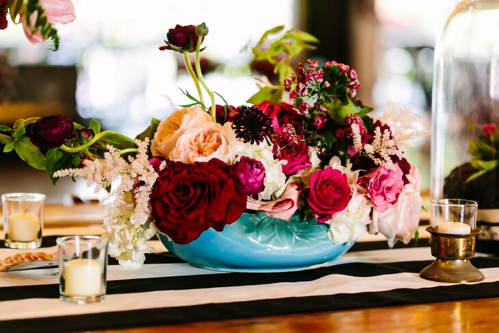 La Tavola Fine Linen provided black-and-white-striped table runners to cover the wooden farm tables at the reception at Pecan Springs Ranch in Austin, Texas. Mismatched vintage vases overflowing with deep red, pink and white blooms added color and whimsy.