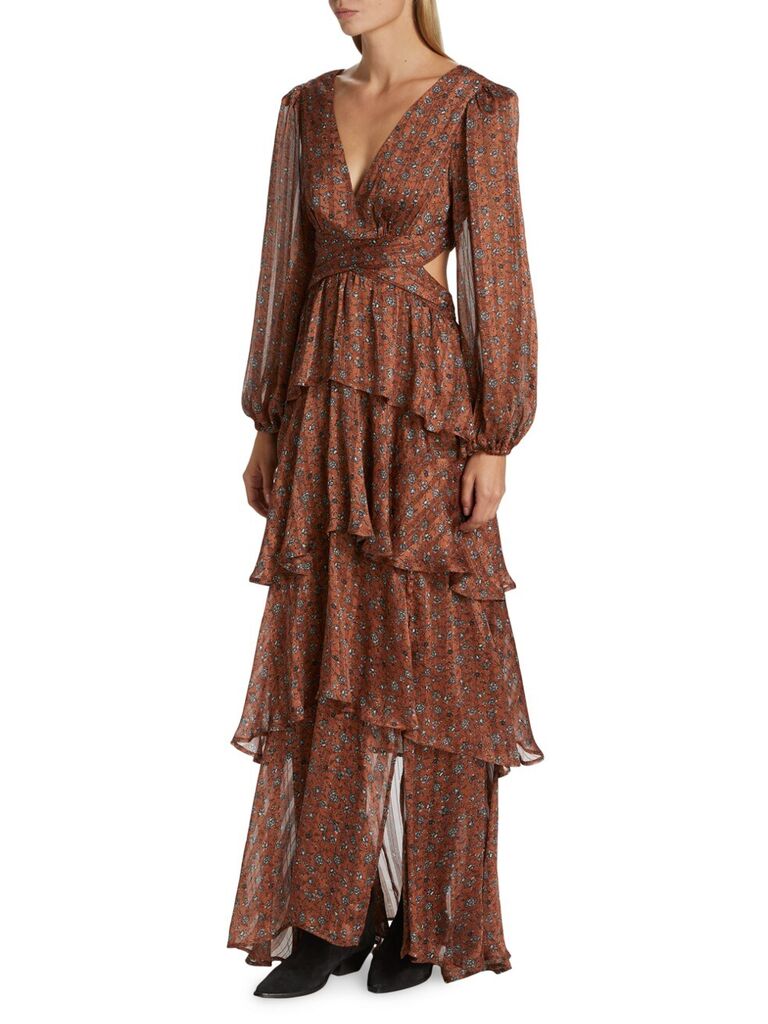 Model wears a ruffled amber dress with long sleeves and a floral print. 