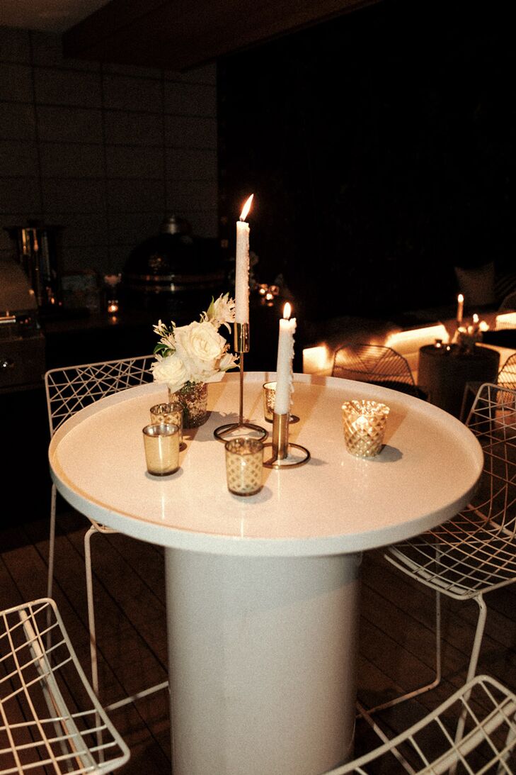 Intimate and elegant small dining cocktail table in white with small gold votives, taller candles and low centerpieces featuring white blooms at Kohi Beach Eatery in New Zealand.