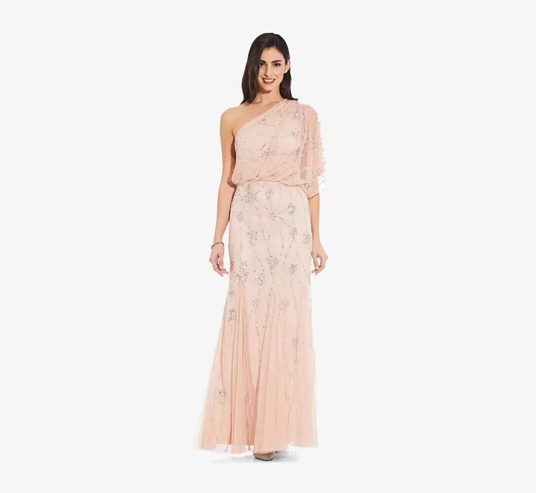 Model wears a blush colored one-shoulder dress with intricate beading. 