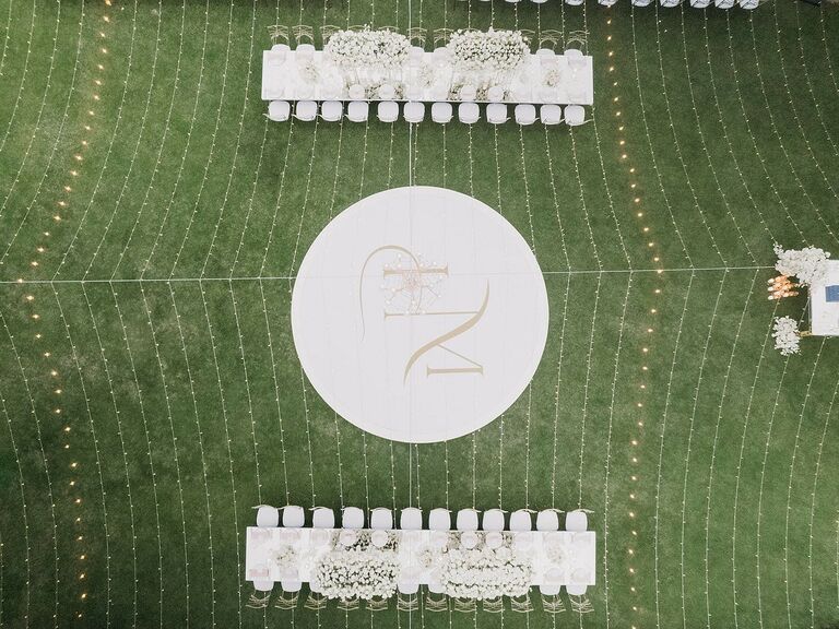 aerial photo of outdoor wedding reception with round monogrammed dance floor under a canopy of string lights