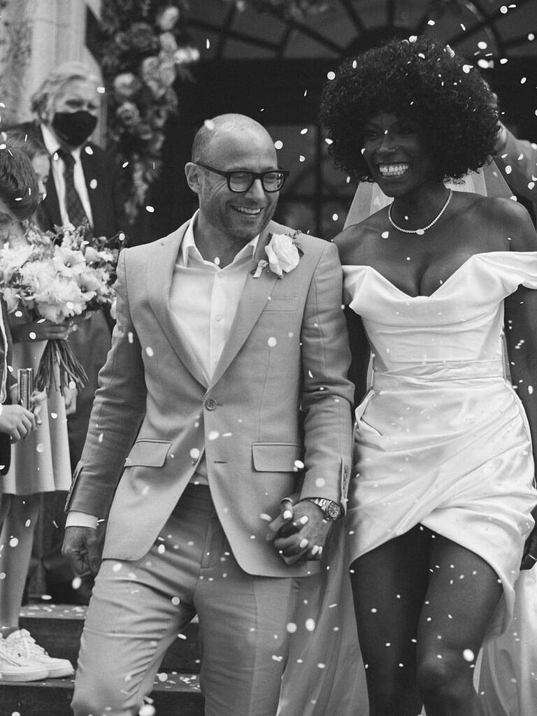 Lorainne Pascal walks hand in hand with her husband while wearing a short white wedding dress. 