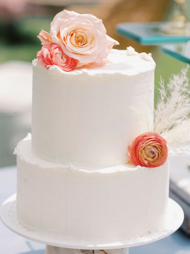 small white wedding cake with ruffled edges, peach rose, orange ranunculus and pampas grass
