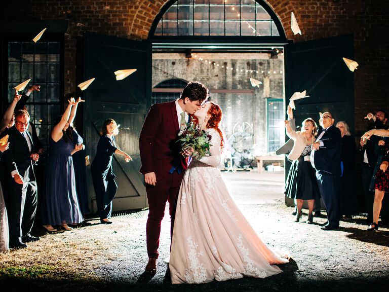 Bride and groom kissing during paper airplane exit toss.