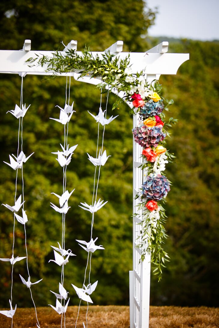 The focal point of the ceremony was a large white trellis, strung up with garlands of white, hand-folded paper cranes and lined with vibrant, rainbow-colored floral arrangements.