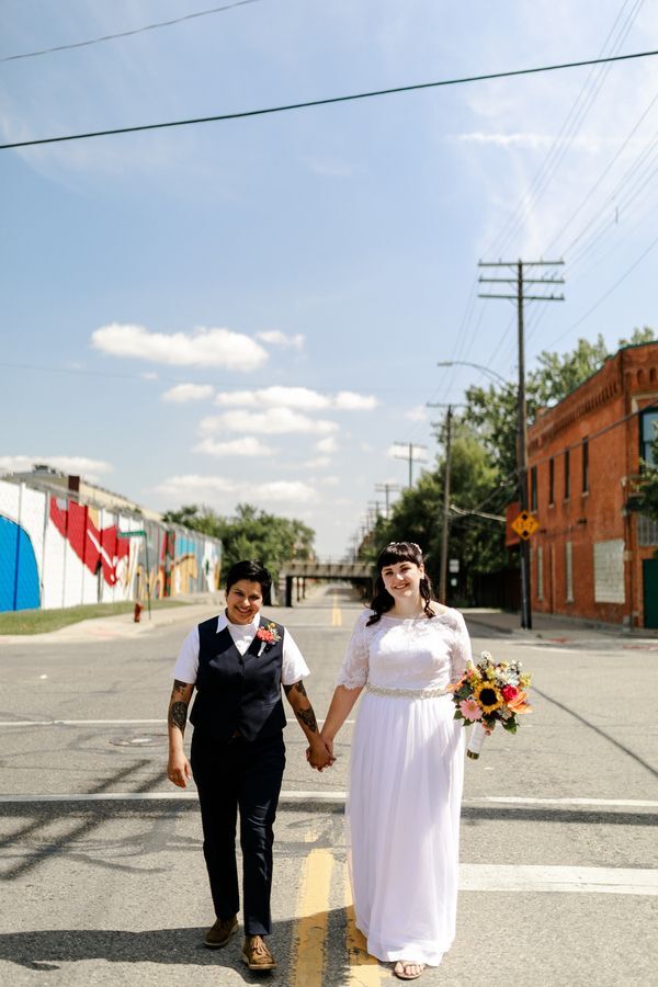 Couple holding hands in the street while posing with sunflower bouquet