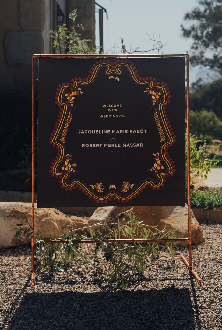 A unique welcome sign to an alternative wedding at a private ranch residence featuring black fabric and red-and-gold embroidery.