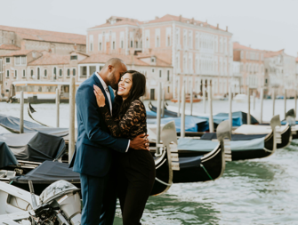 Man in blue suit and woman in black floral lace top embracing after proposal