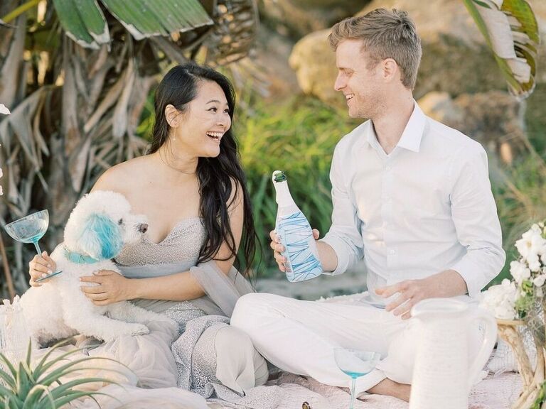 Couple sharing champagne toast on the beach with their dog