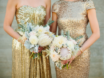 Two maids of honor in gold sparkly dresses holding bouquets