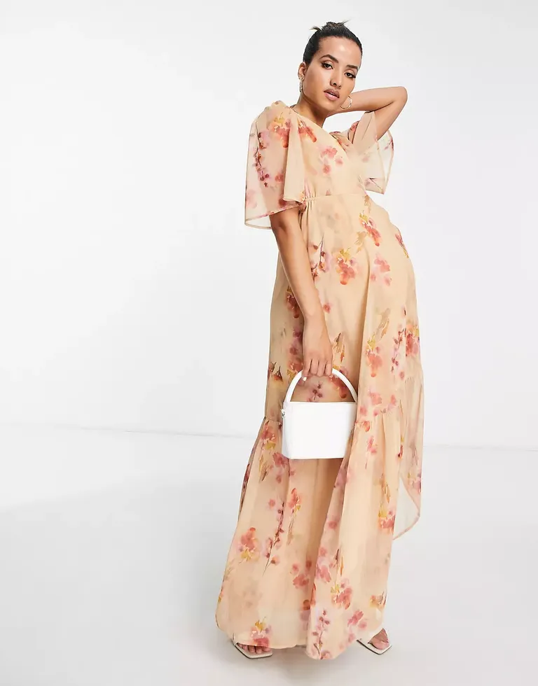 Model wears a flowy peach dress with a pink floral pattern. 