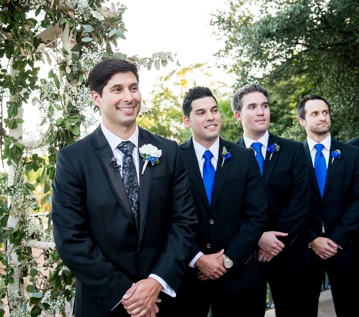 The groomsmen wore black suits with matching cobalt blue ties and boutonnieres. John stood apart—he wore a patterned tie with a white boutonniere.