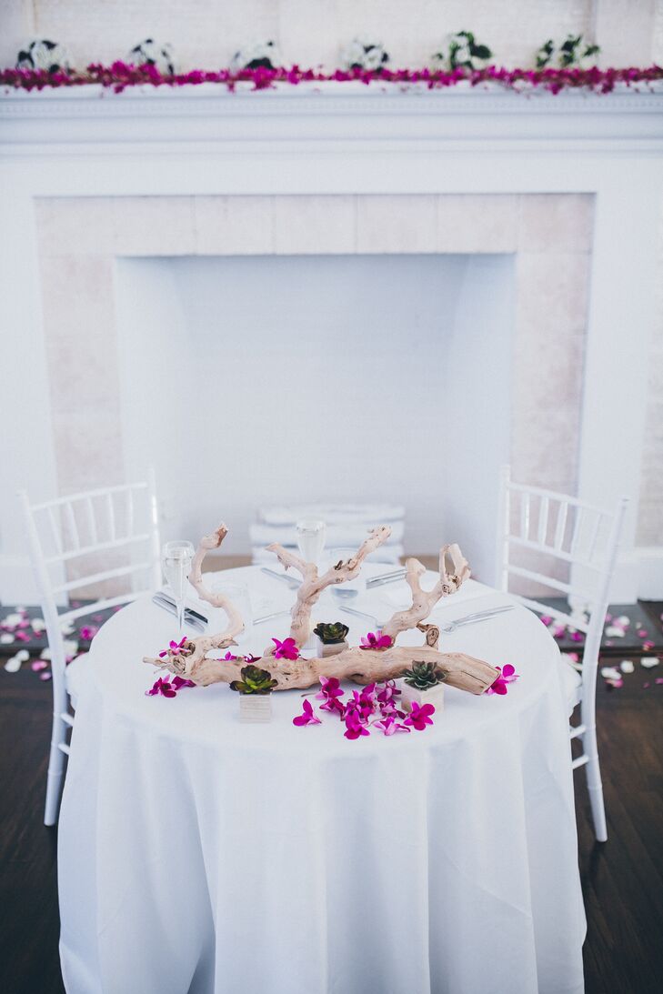 Simple arrangements of driftwood and fuchsia flowers decorated the couple's all-white sweetheart table.