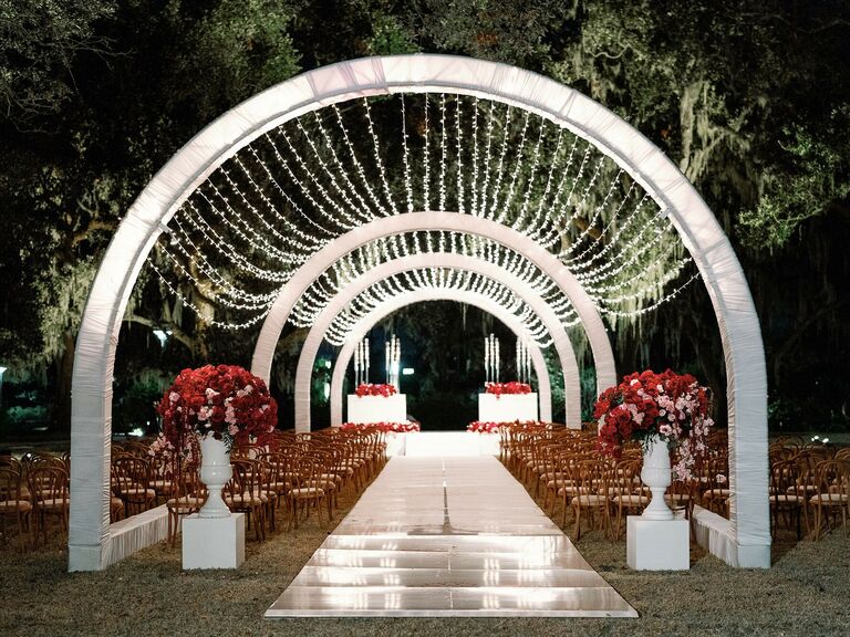outdoor wedding ceremony at night with arched tunnel and string light canopy above the aisle