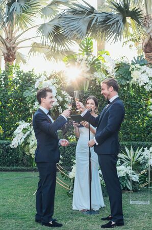 Grooms in Matching Tuxedos Toasting at Wedding Ceremony, Tropical Arch