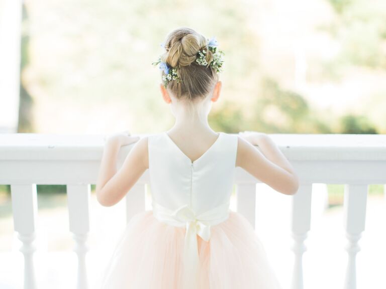 Flower girl wears her hair in a top knot adored with fresh flowers. 