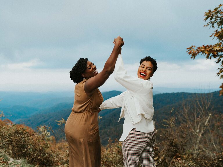 Two women laugh together with mountains in the background for their engagement photo
