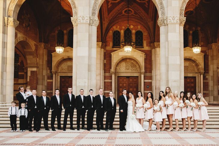 The married couple stood with their wedding party, who were dressed in black and blush attire. The groomsmen sported black tuxedos, and the bridesmaids wore blush short dresses.