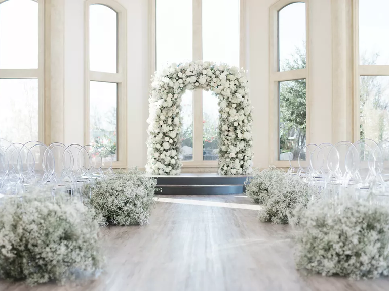 A baby's breath wedding arch stands at the end of a modern wedding aisle.