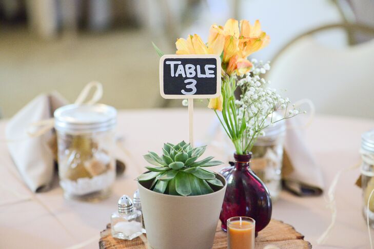 Each centerpiece brought their natural setting inside the Lakeside Clubhouse ballroom. They highlighted every neutral linen with potted succulents, bright yellow tulips and baby’s breath inside mixed bulb vases. A wooden base and low tealight candles added to the organic feel. Guests found their seats with the help of a chalkboard number protruding from the succulent.