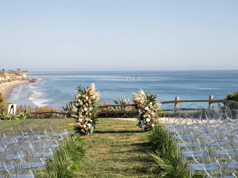 An outdoor wedding ceremony site by the ocean, with a vibrant floral arrangement at the top of the aisle.