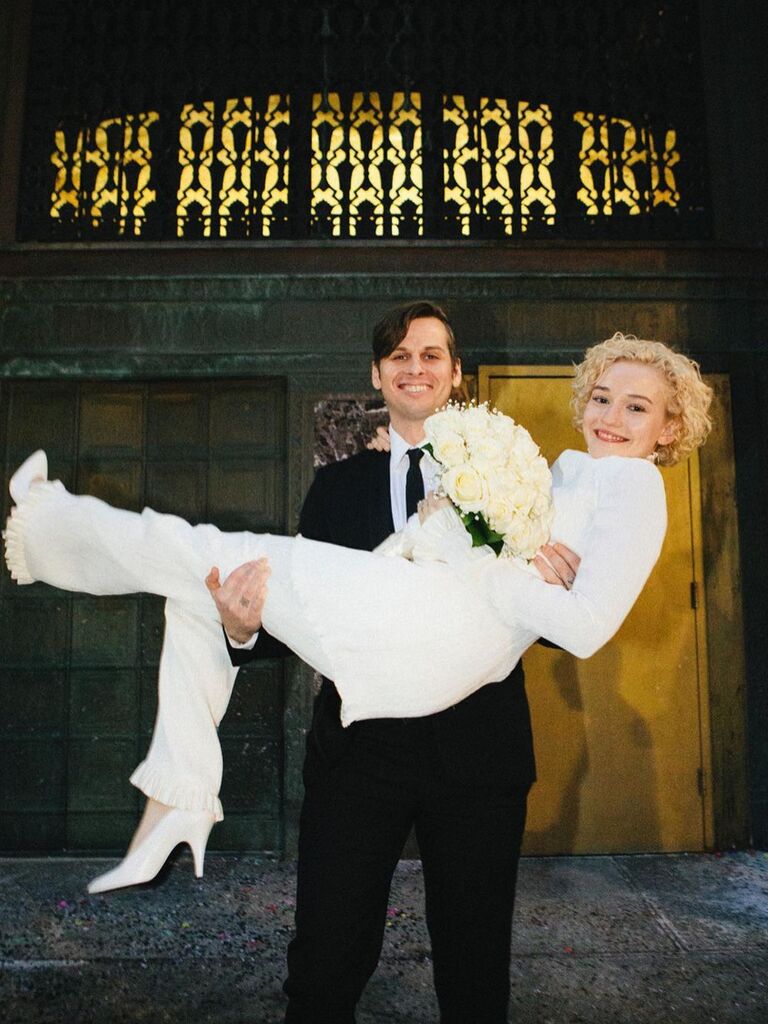 Julia Garner is held by her husband while wearing a chic white wedding suit. 
