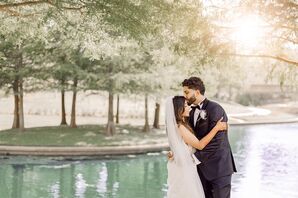 Groom in Dark Navy Tuxedo Kissing Bride With Long Veil on Forehead in Front of a Lake