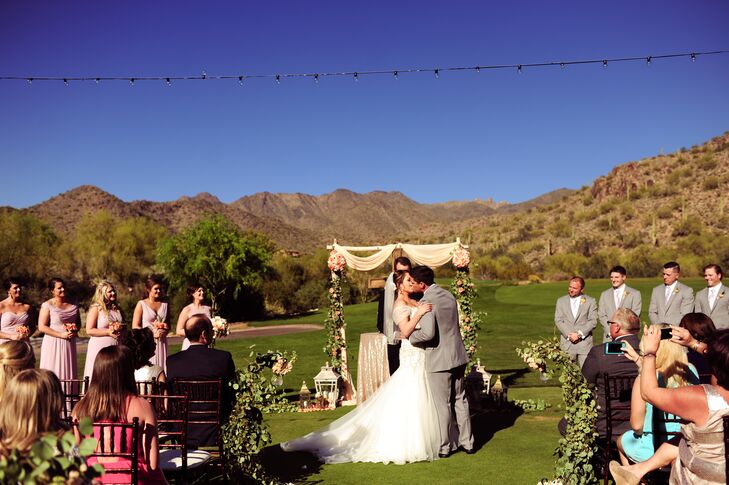 Sheer, peach fabric and a eucalyptus garland draped across the birch wedding arch with groupings of coral roses and dahlias completed the warm, romantic wedding style.