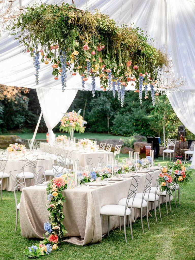 long wedding reception table with garden-inspired hanging centerpiece of blue delphinium, greenery, pink dahlias and yellow roses