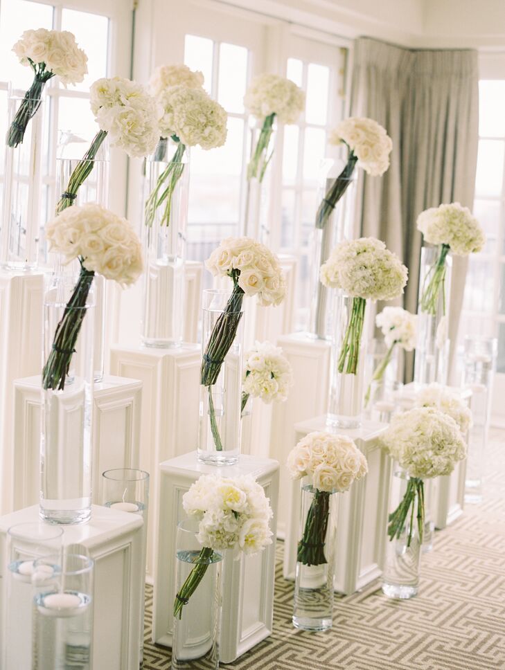 Long-stemmed bunches of white flowers in glass pillar vases were placed on white pedestals of varying heights to create the couple's one-of-a-kind ceremony backdrop at the Hay-Adams in Washington, DC.