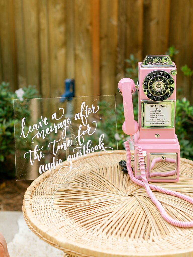2023 wedding reception trend telephone wedding guest book with pink vintage rotary phone and acrylic calligraphy sign that says leave a message after the tone